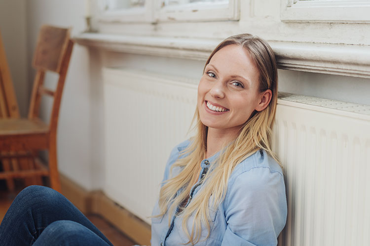 Frau sitzt angelehnt an einem Heizkörper